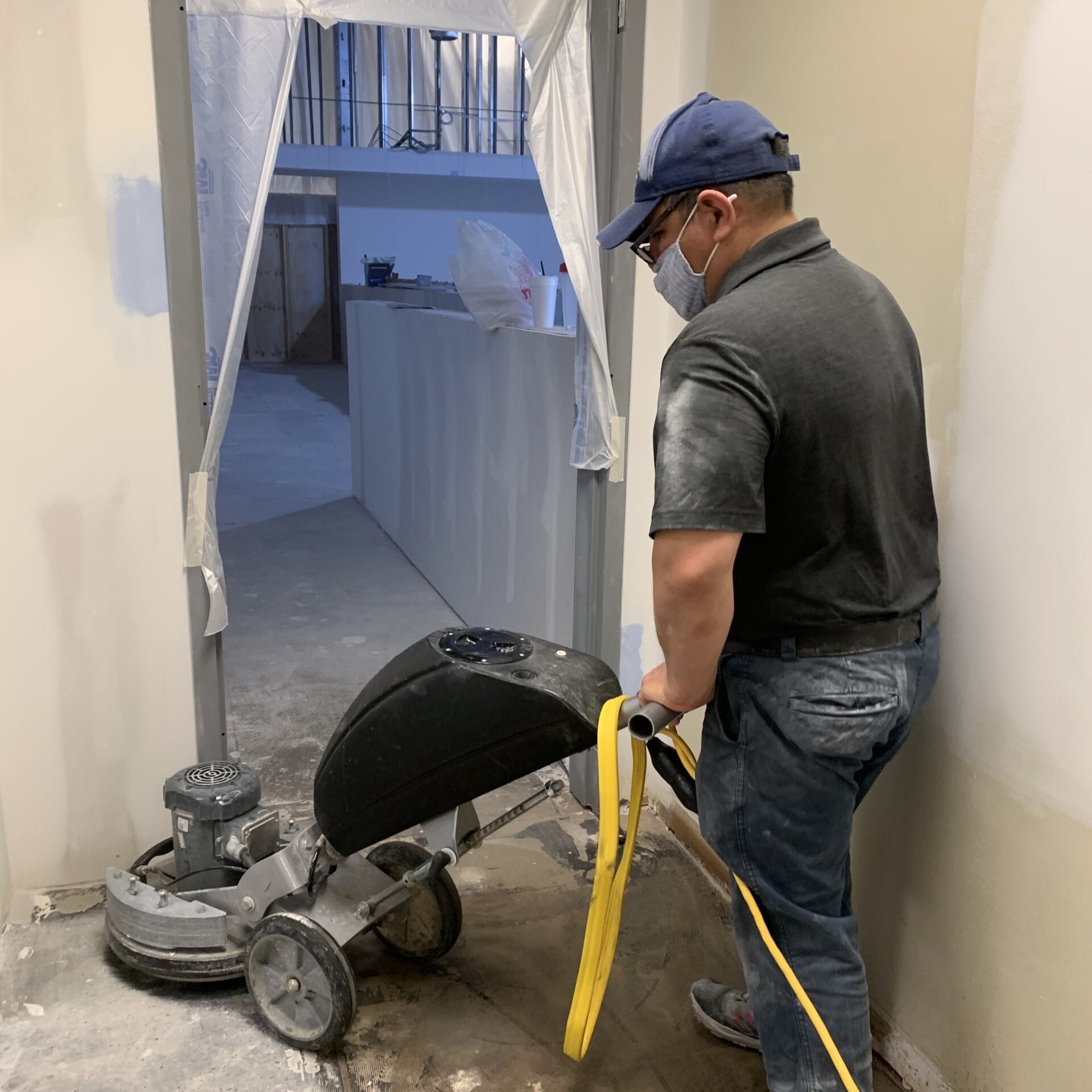 Man using a floor grinder on a concrete floor in a construction site. Dust visible.
